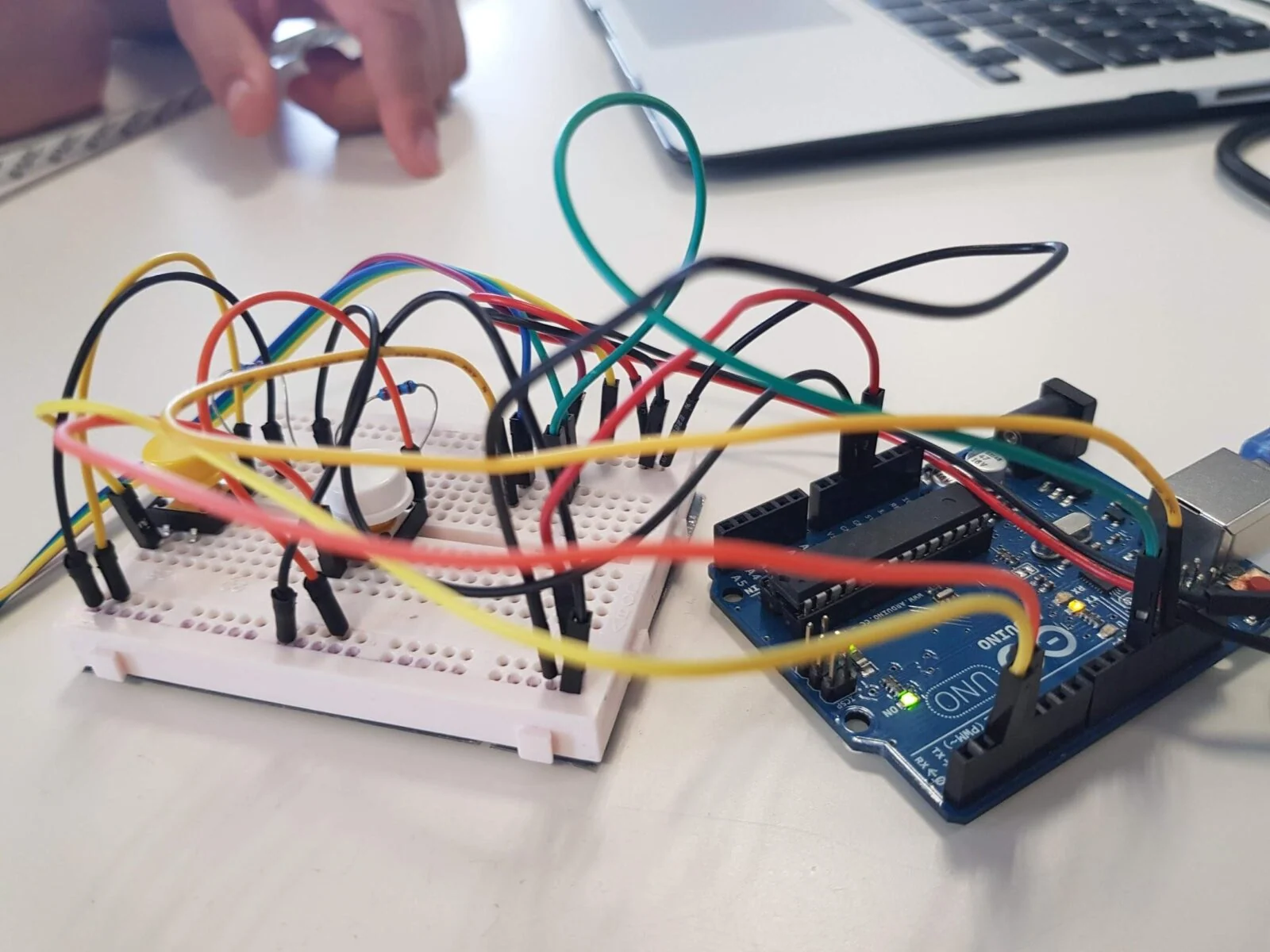 Płytka Arduino połączona kolorowymi przewodami z płytką stykową obok laptopa.