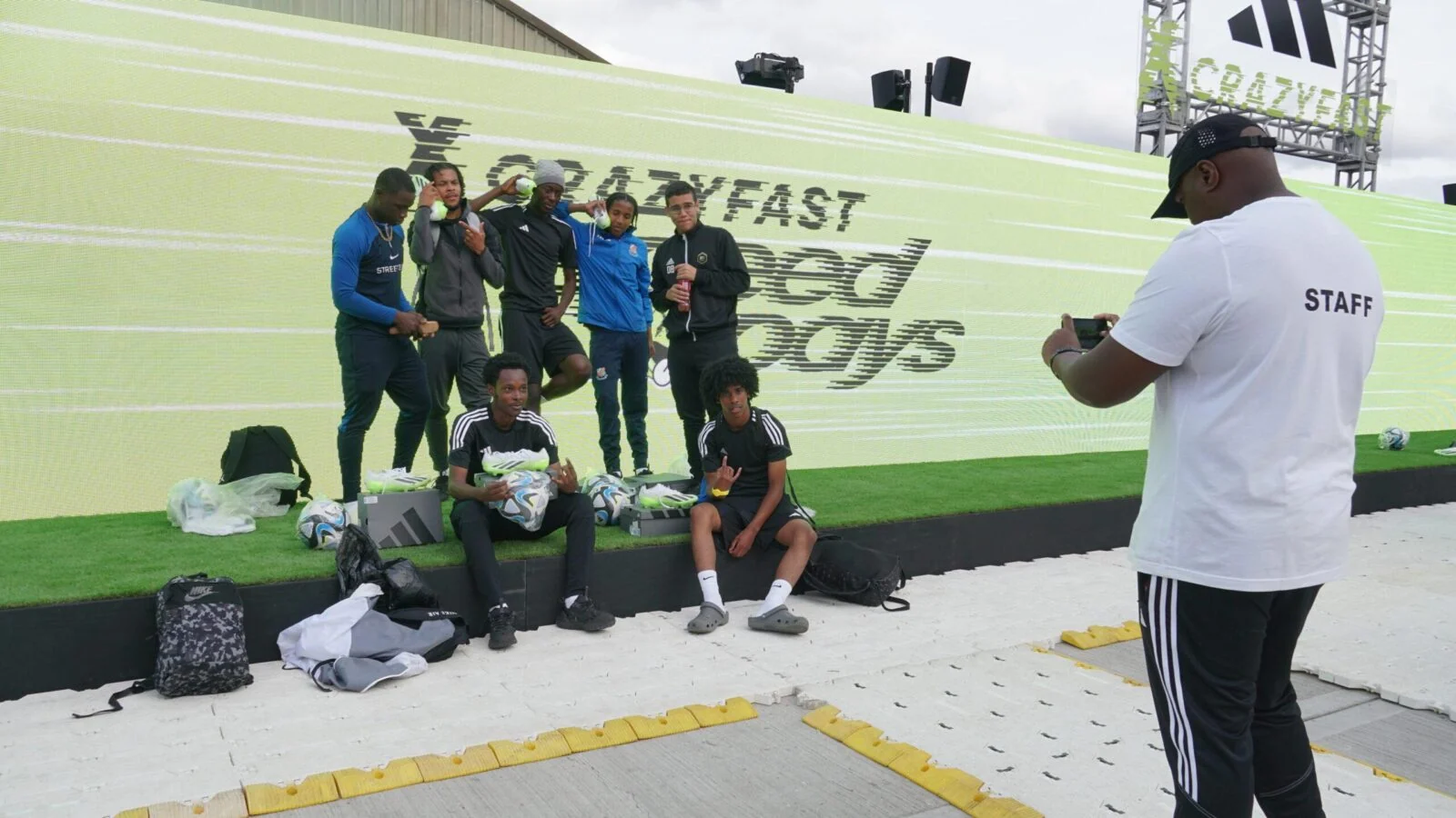 Grupa z piłkami pozuje przed ekranem Adidas Crazyfast, a pracownik robi zdjęcie.