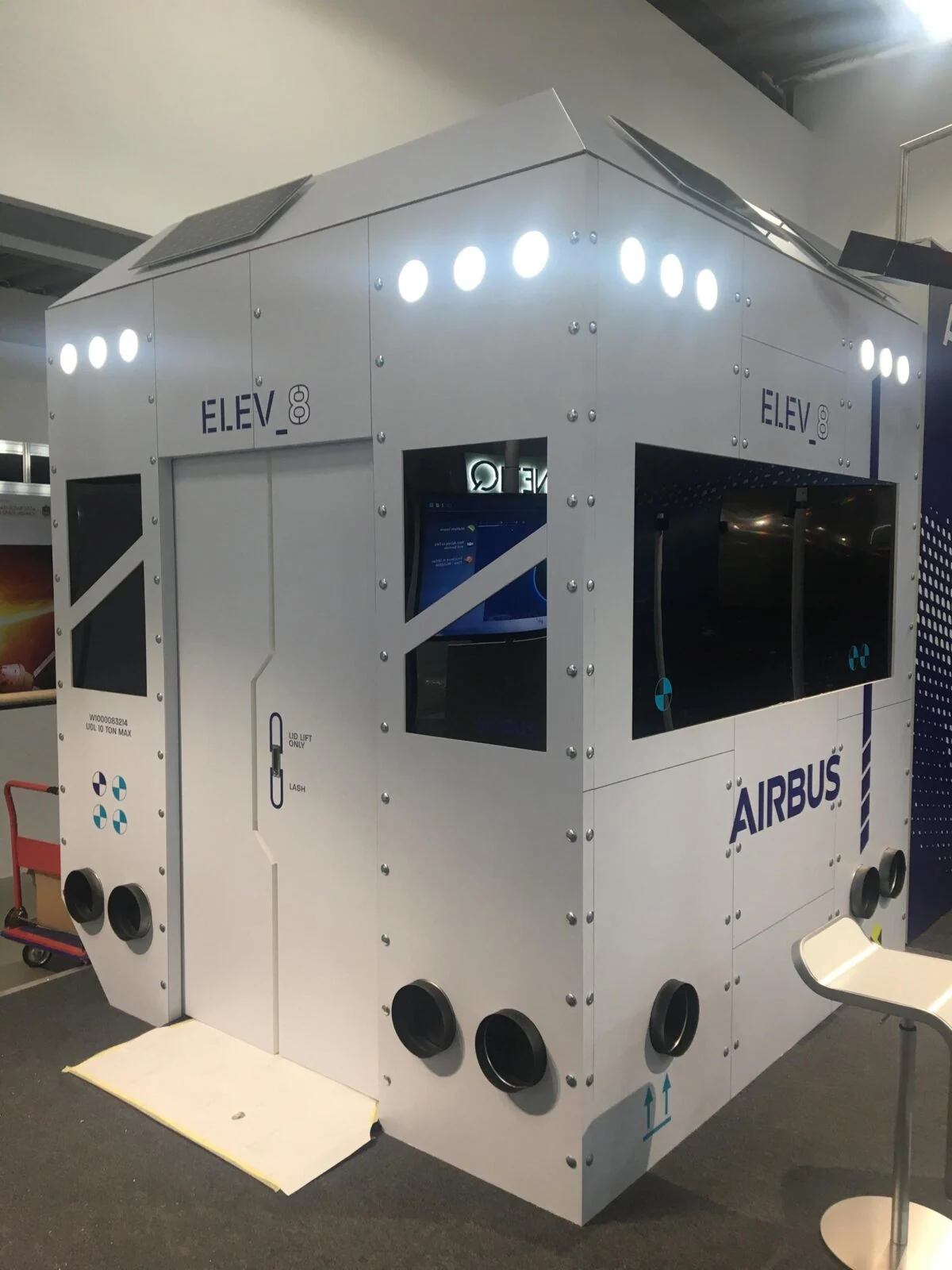 Biała kabina wystawowa Airbus ELEV8 z podświetlonymi górnymi panelami i wbudowanymi ekranami.