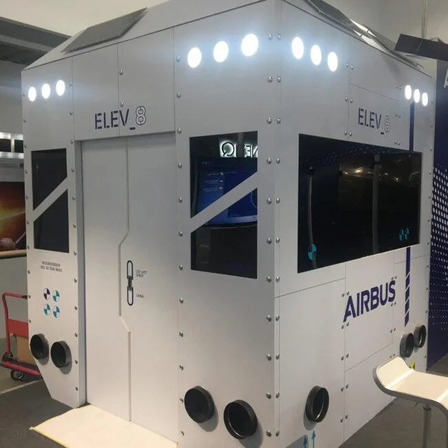 Biała kabina wystawowa Airbus ELEV8 z podświetlonymi górnymi panelami i wbudowanymi ekranami.