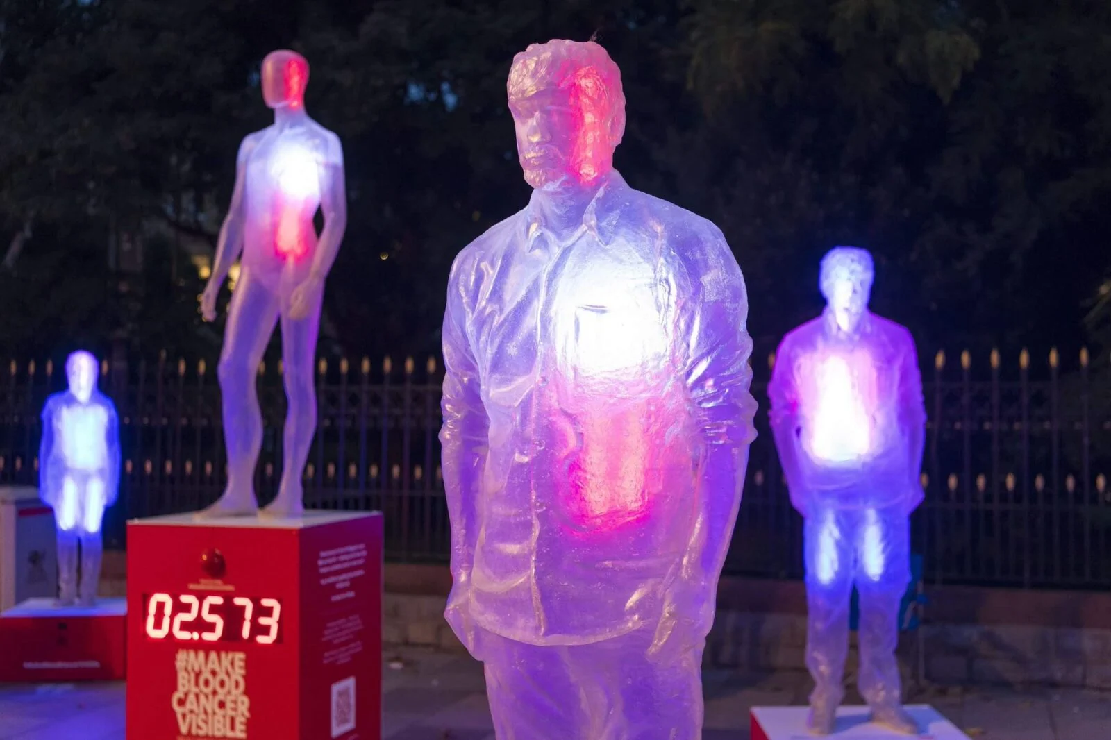 Półprzezroczyste postacie ludzkie podświetlone na różowo i niebiesko w instalacji Make Blood Cancer Visible.