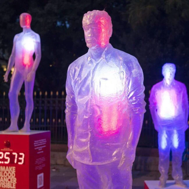 Półprzezroczyste postacie ludzkie podświetlone na różowo i niebiesko w instalacji Make Blood Cancer Visible.