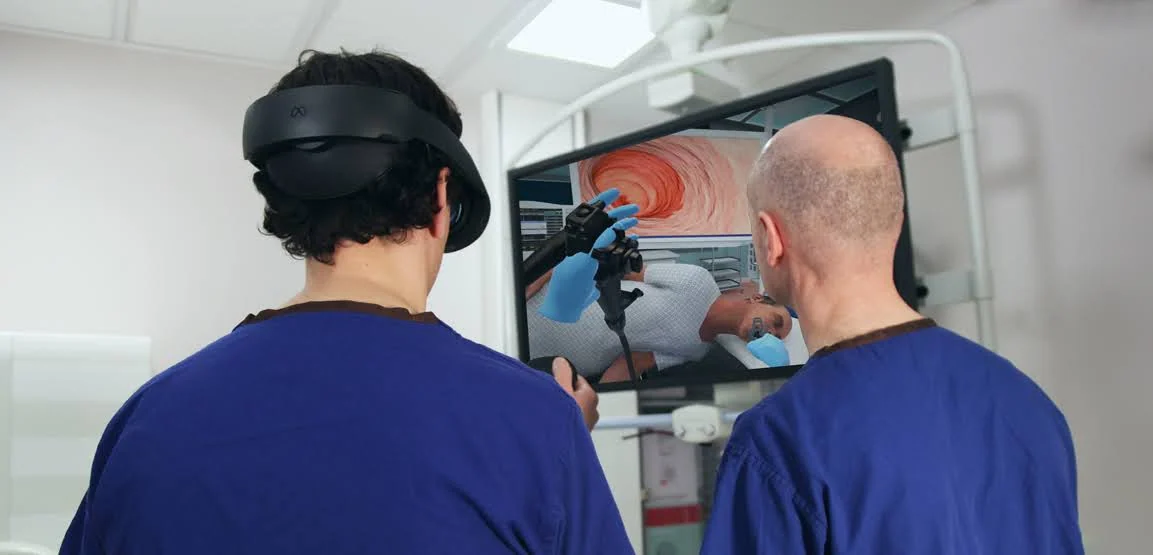 Dwie osoby w niebieskich strojach medycznych analizują na monitorze symulację endoskopii VR.