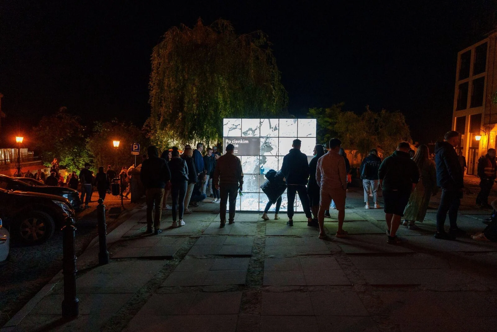 Zwiedzający wokół podświetlonych paneli wystawowych na placu nocą.