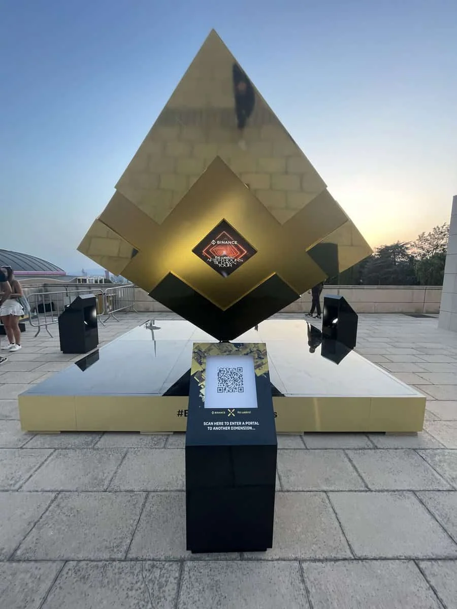 Złota geometryczna rzeźba Binance z postumentem z kodem QR na placu.