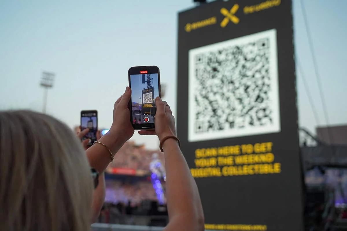 Uczestnik koncertu skanuje kod QR z ekranu wydarzenia Binance i The Weeknd.