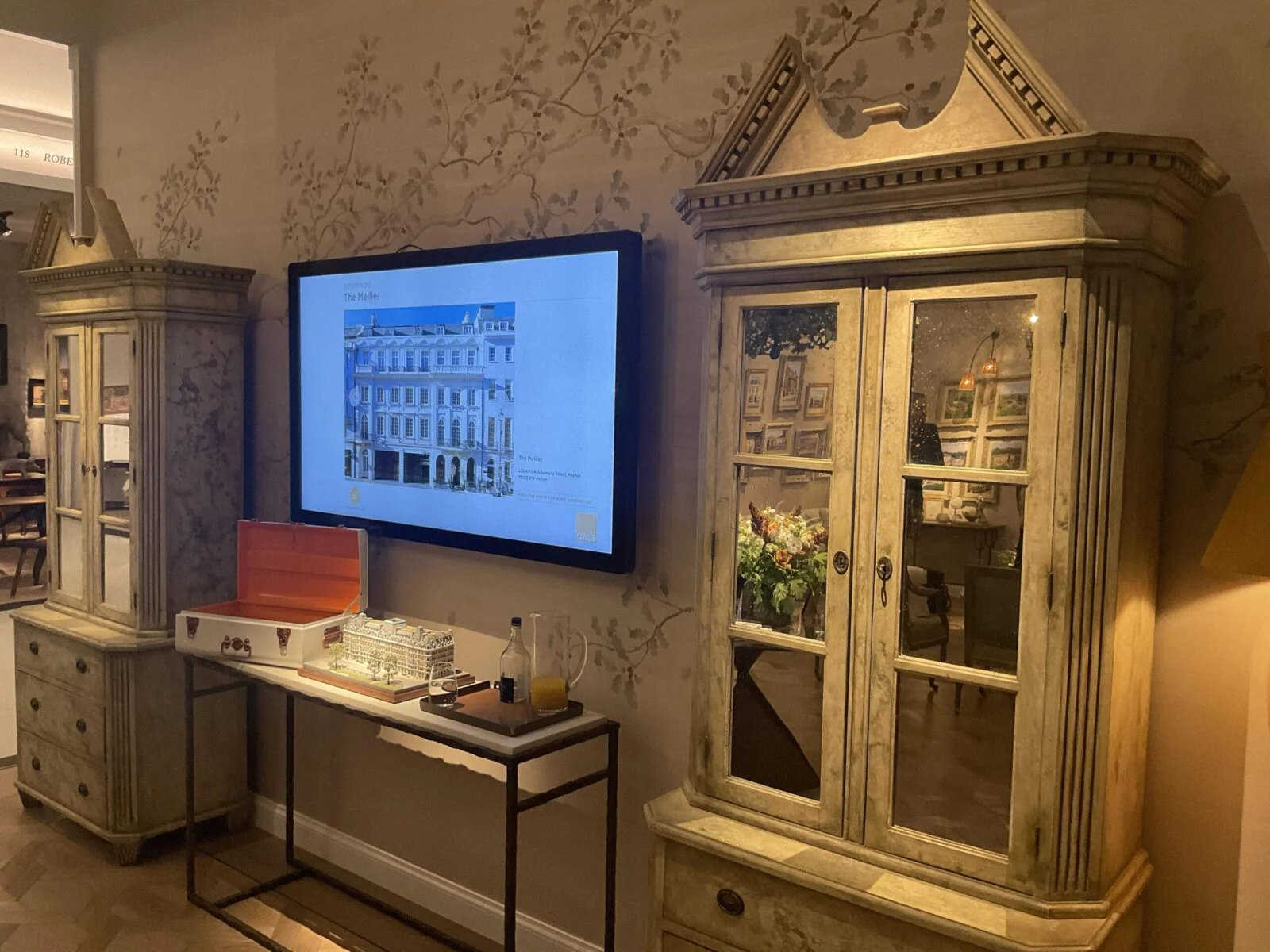 Zdjęcie architektury na ekranie ściennym nad miniaturami budynków na Masterpiece Fair.