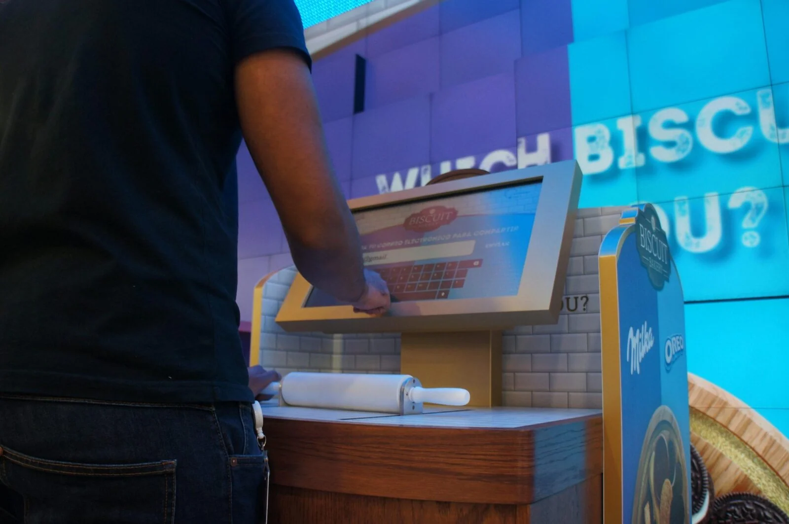 Zbliżenie osoby korzystającej z kiosku Mondelez z wałkiem do ciasta pod ekranem dotykowym.