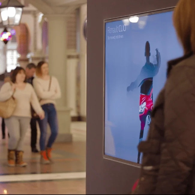 Uczestnik przed ekranem z awatarem Renault podczas aktywacji w zatłoczonym centrum handlowym.