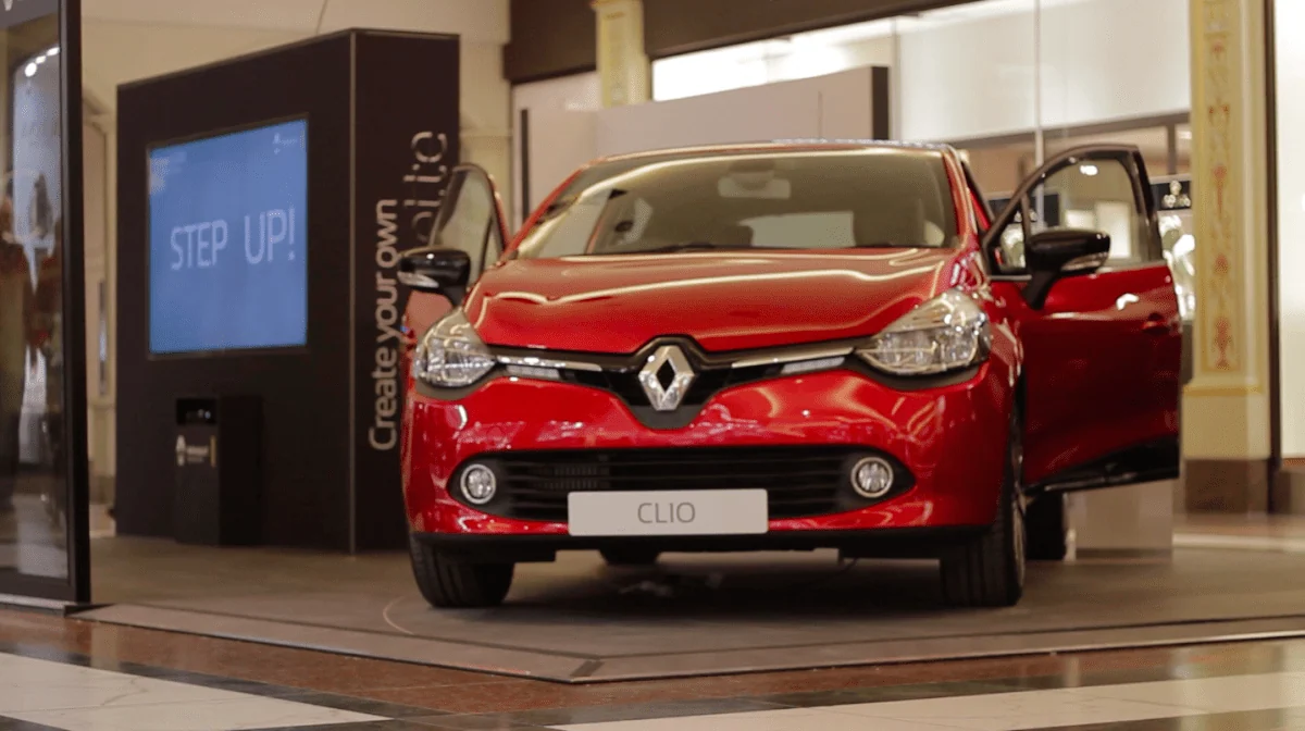 Czerwone Renault Clio obok interaktywnego kiosku Step Up w centrum handlowym.