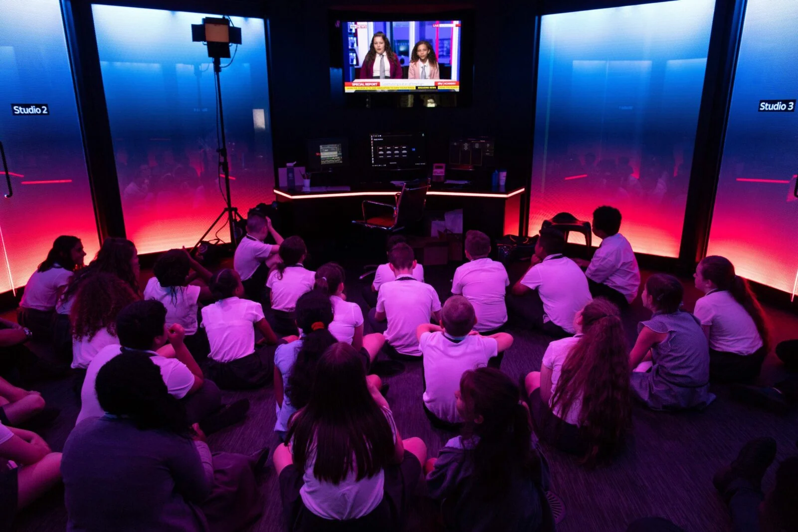 Dzieci siedzą na podłodze i oglądają monitor w jasno oświetlonym studiu Sky Academy.