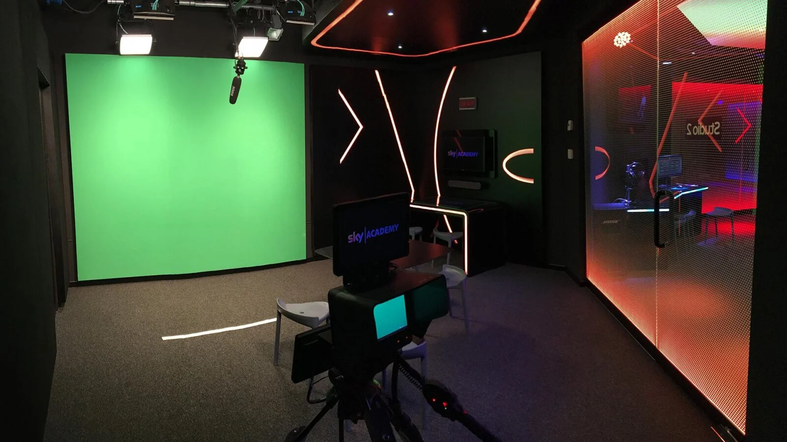 Kamera studyjna skierowana na green screen pod lampami i mikrofonem na wysięgniku.