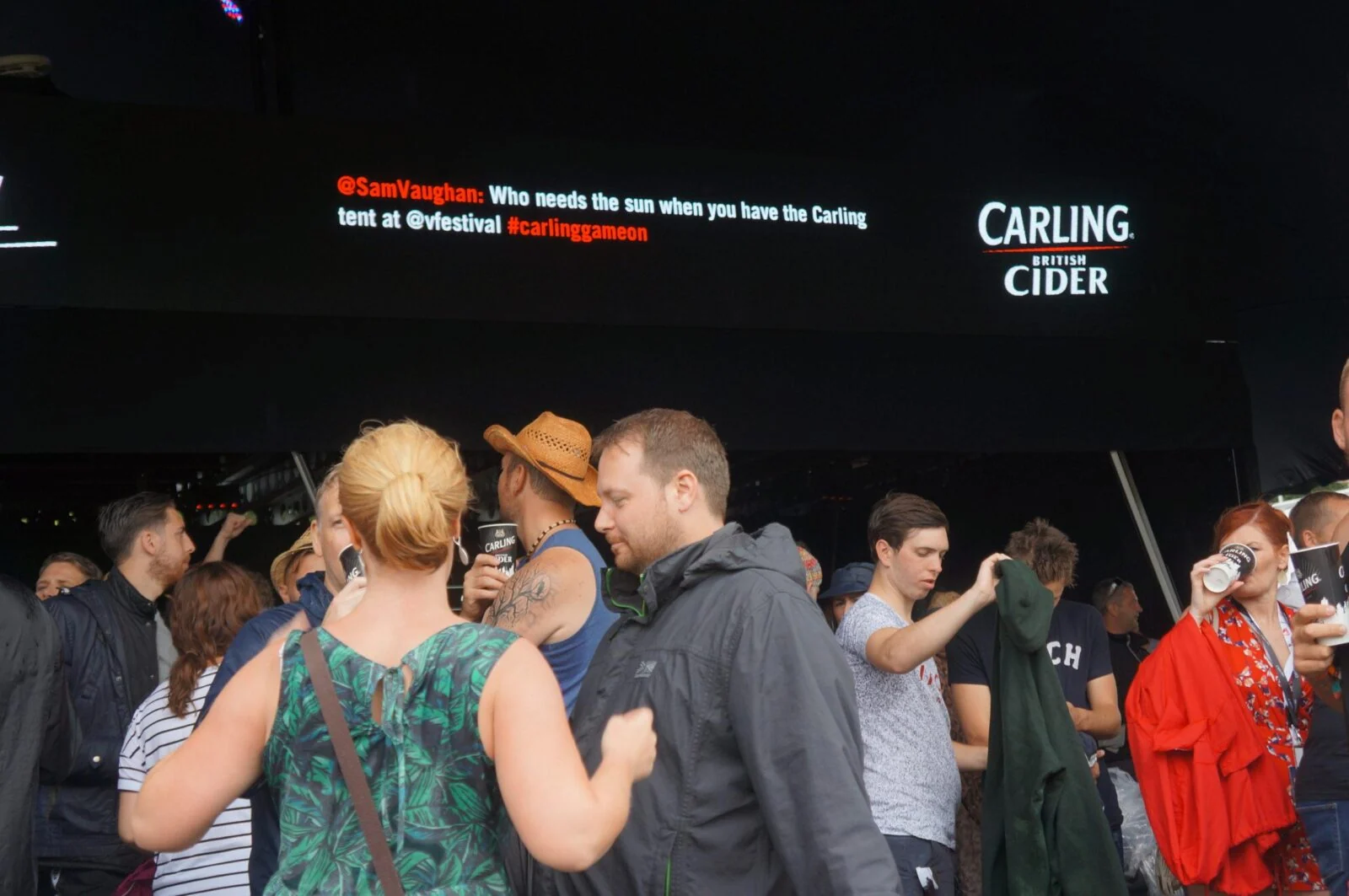 Logo Festival bar visitors beneath a screen displaying a social media message and Carling Cider.