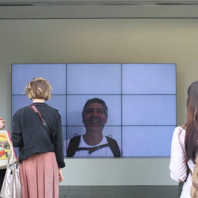 Zwiedzający przed ekranem Smiles Film w Serpentine Gallery.